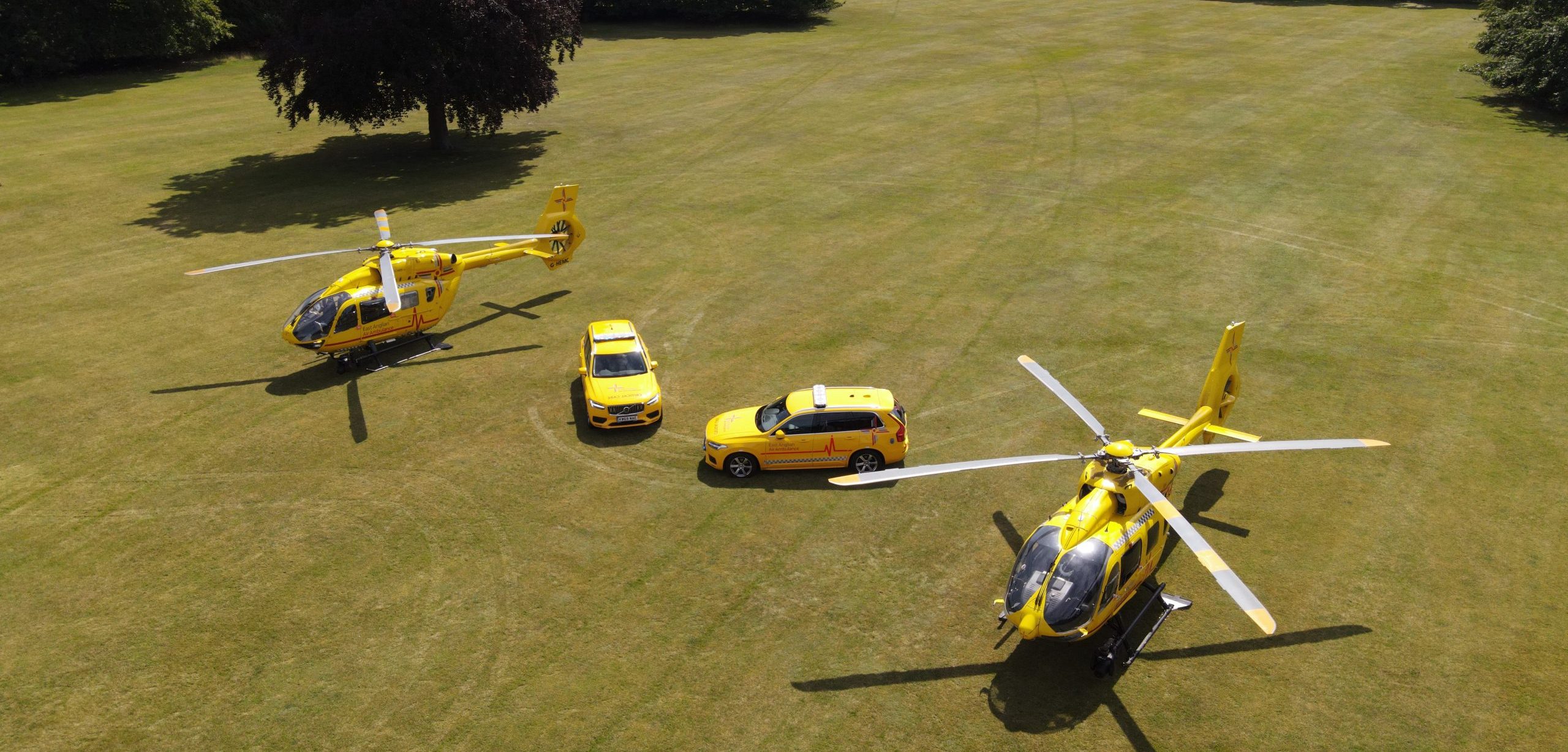 EAAA's two helicopters and critical care cars parked next to each other on grass