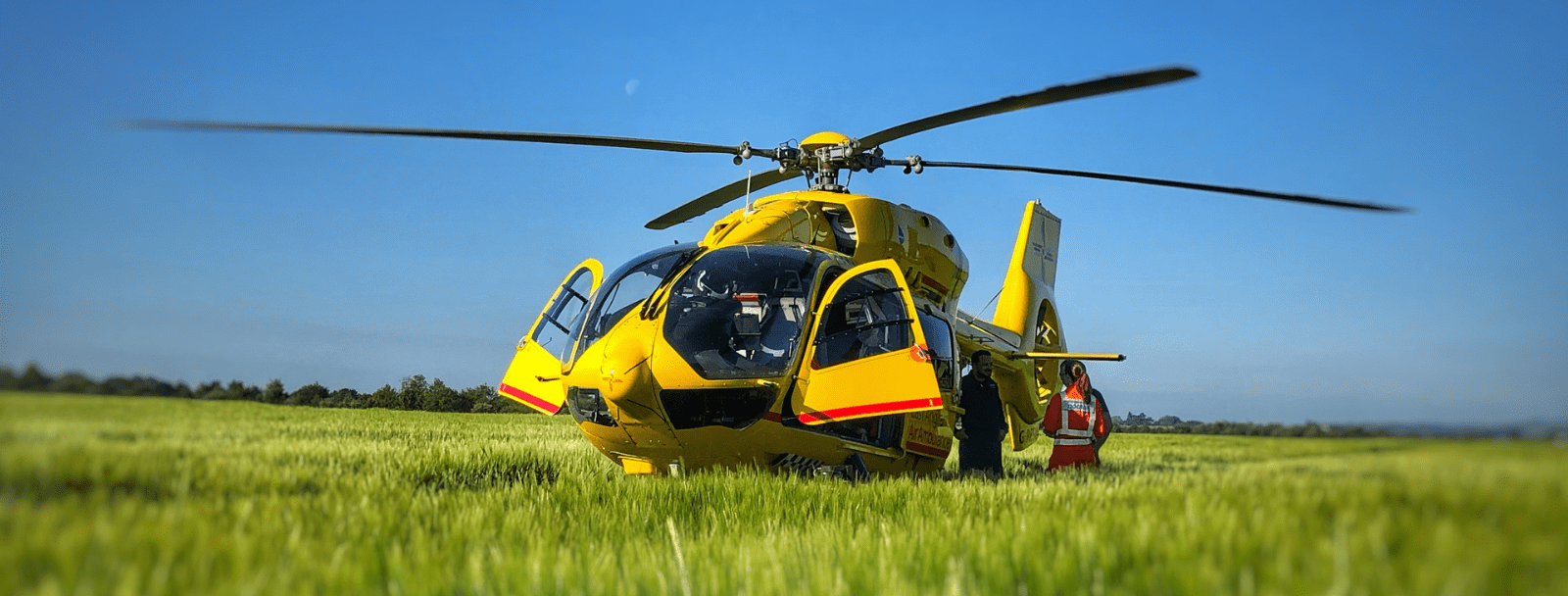 Yellow, EAAA helicopter in a green field with doors open