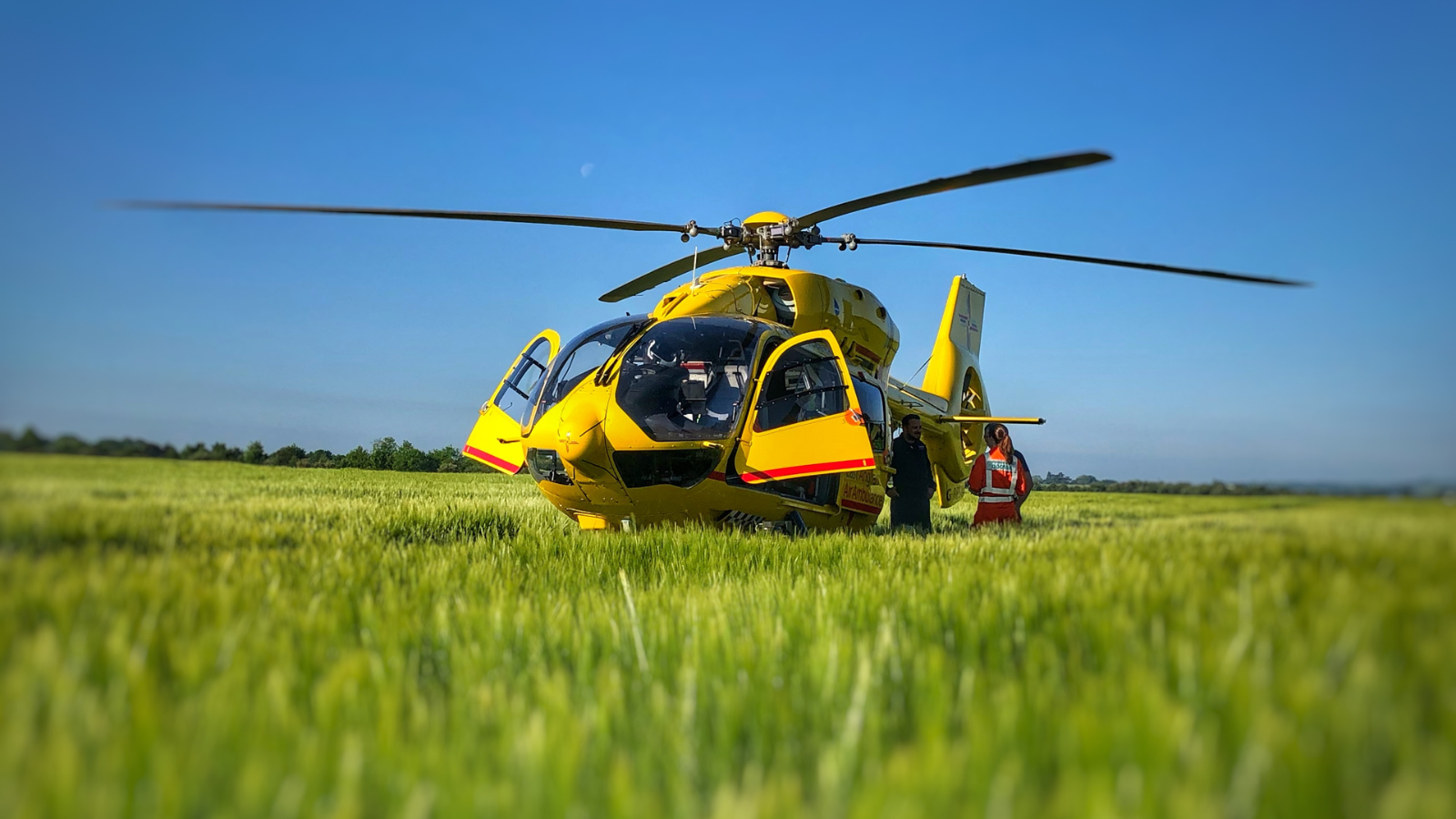 Yellow, EAAA helicopter in a green field with doors open