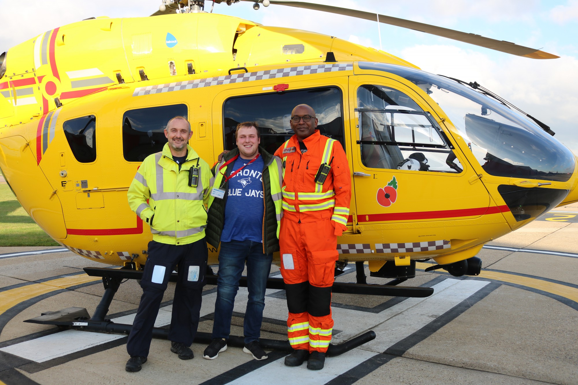 Jordan Greenwood in front of the EAAA helicopter with Pilot Steve Norris and Dr Victor Inyang.