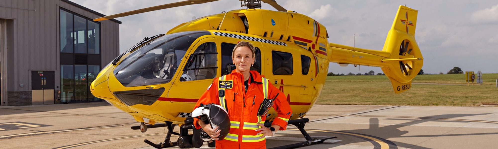 Dr Kate Mead standing in front of helicopter in flight suit